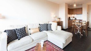 A modern living room with a sectional sofa, a coffee table, and a dining area with wooden chairs and a table.