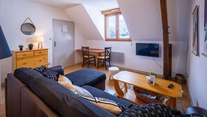 Ein gemütliches Wohnzimmer mit einer Couch, einem Holzesstisch und einem an der Wand montierten Fernseher.