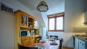 Eine kleine Küche mit Holzausstattung, einem Esstisch und Stühlen. Es gibt eine Mikrowelle, eine Kaffeemaschine und einen Kühlschrank. Ein Fenster sorgt für natürliches Licht.