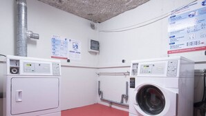 Une buanderie avec deux machines à laver blanches, un sol rouge et des affiches informatives accrochées aux murs.