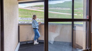 A woman standing by a window on a balcony with a view of a green landscape and a road.