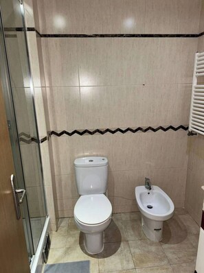 Ein Badezimmer mit zwei Toiletten, einem Bidet und einer Duschkabine aus Glas.