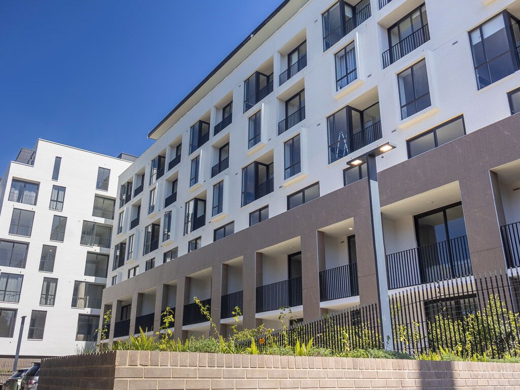 A multi-story residential building with balconies, a brick base, and a clear sky.
