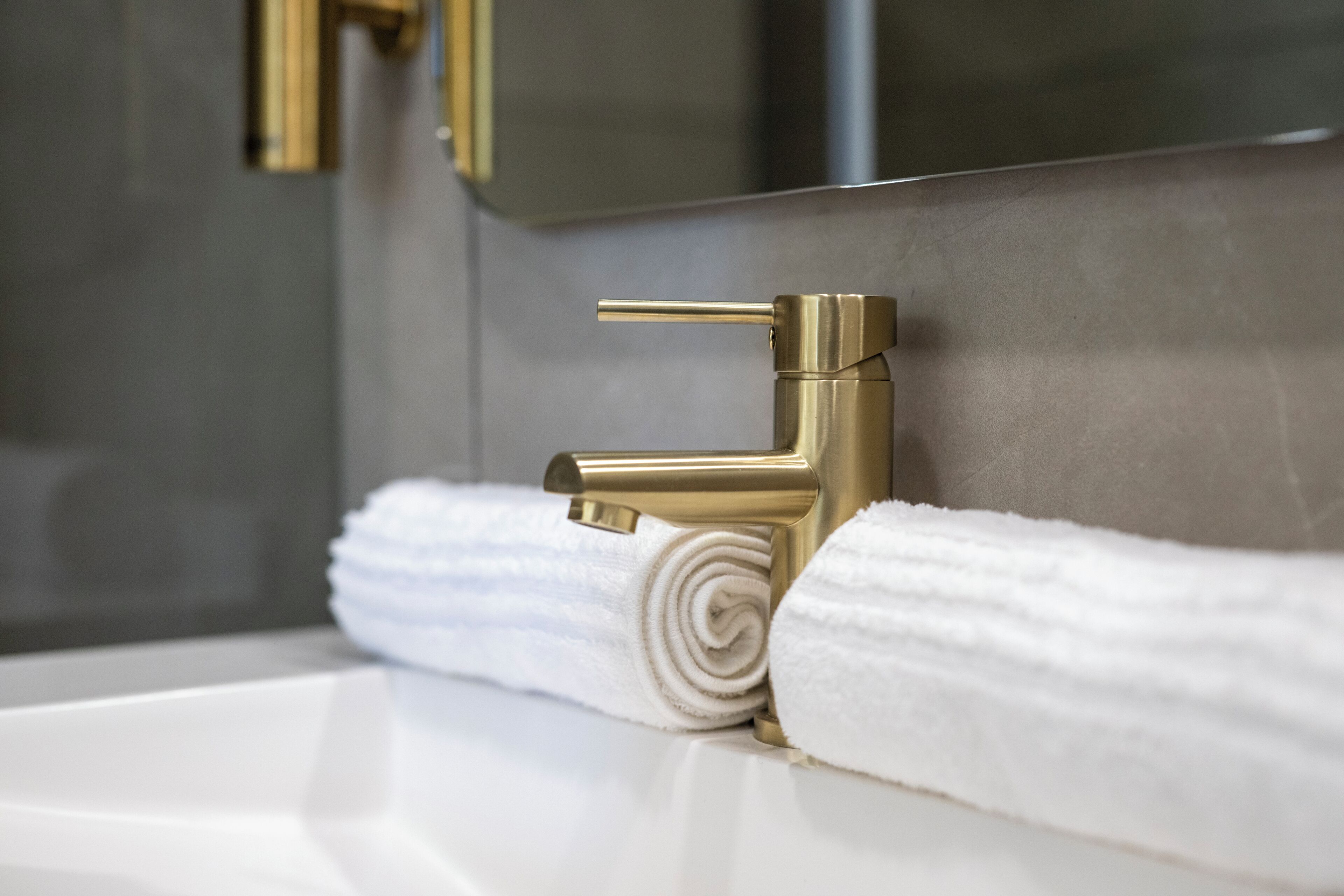 Une salle de bain avec un robinet doré, des serviettes blanches et un miroir.