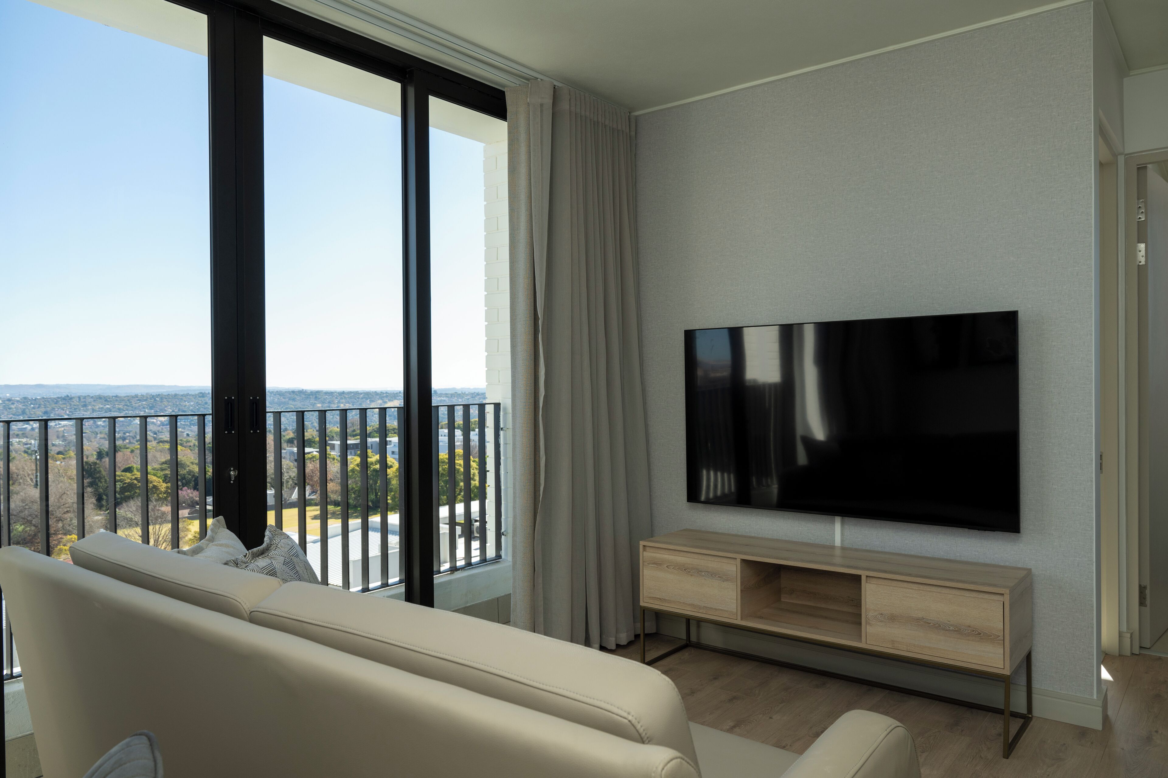 A modern living room with a large flat-screen TV, a beige sofa, and a wooden TV stand.