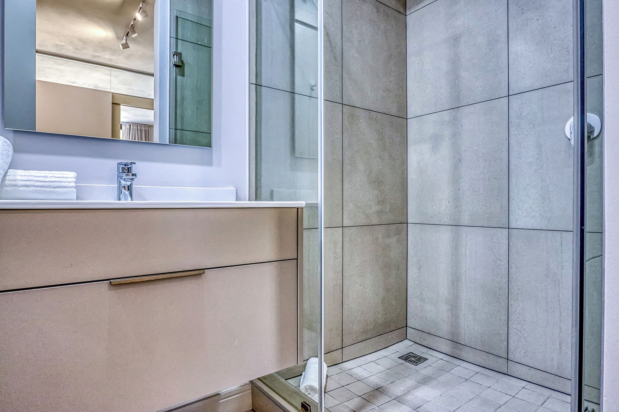 Un baño moderno con cabina de ducha de vidrio, tocador blanco y un espejo grande.