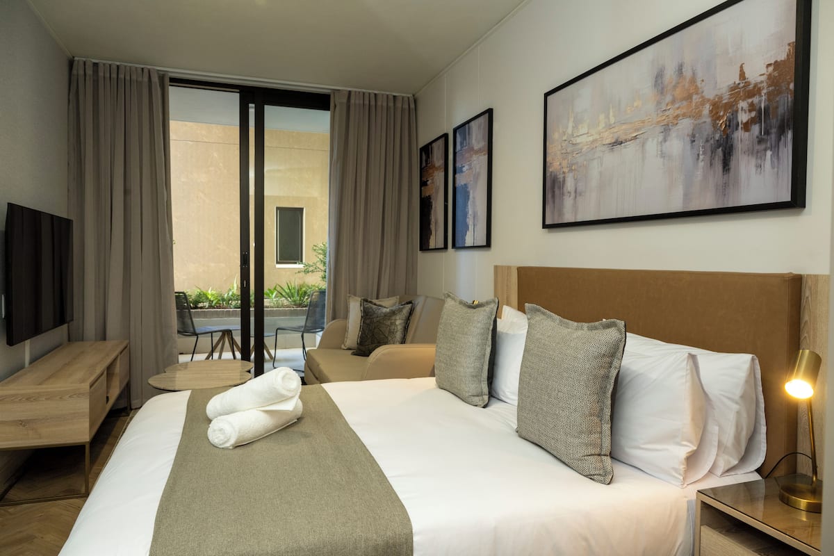 A hotel room with a large bed, a desk, a chair, and a view of the outdoors.