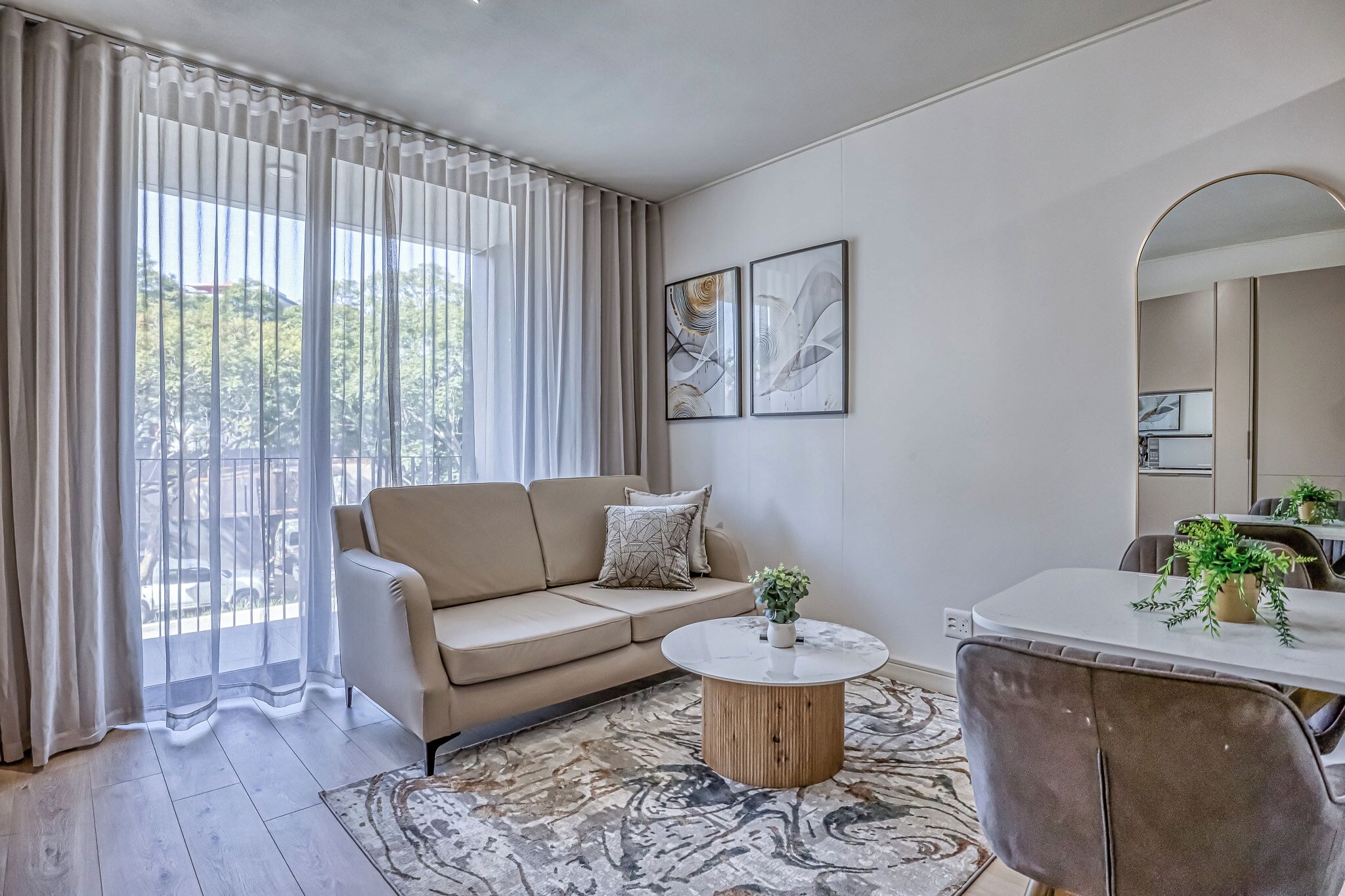 A modern living room with a beige sofa, a round coffee table, and a dining area with a white table and chairs.