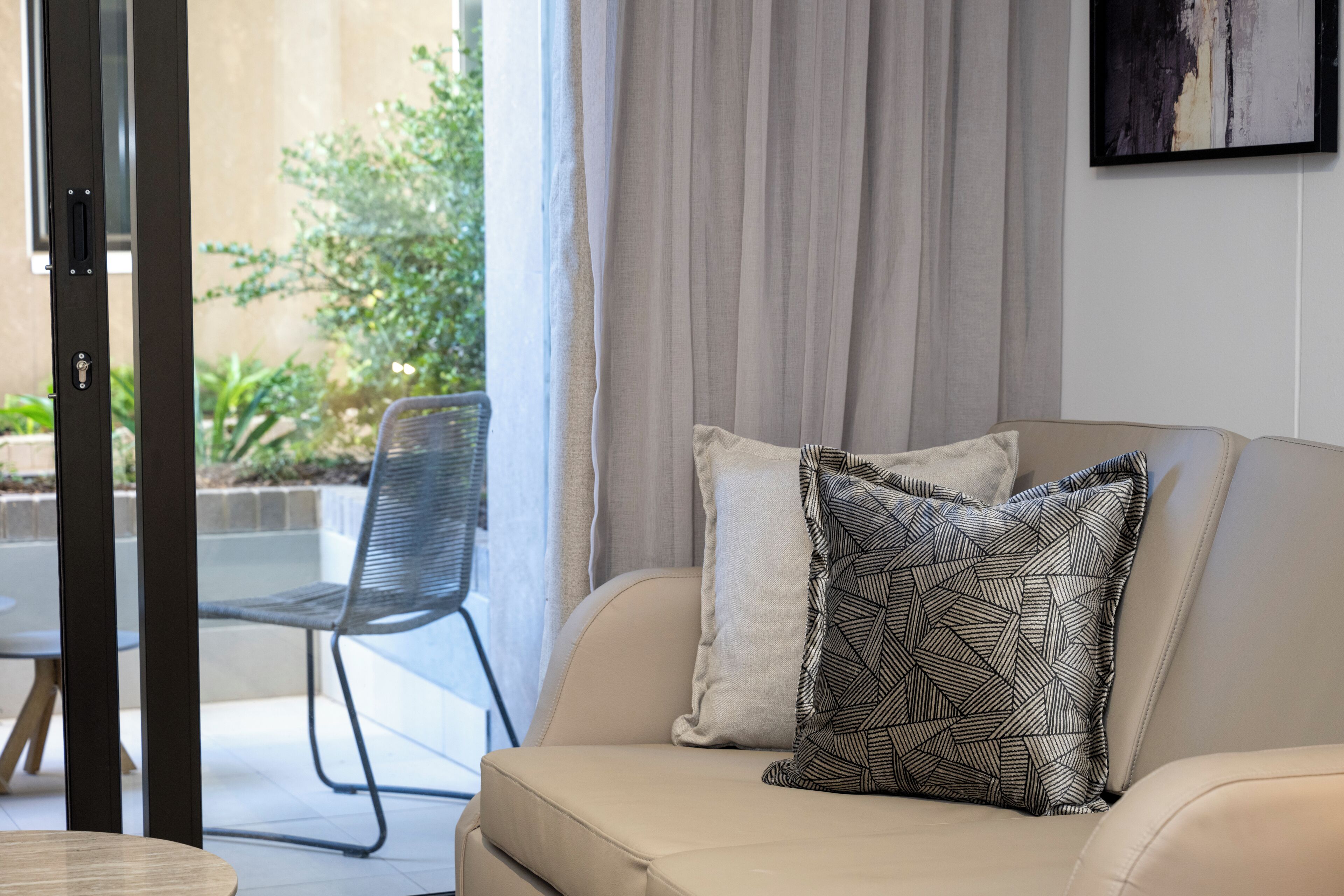A modern living room with a beige sofa, a patterned pillow, and a metal chair.