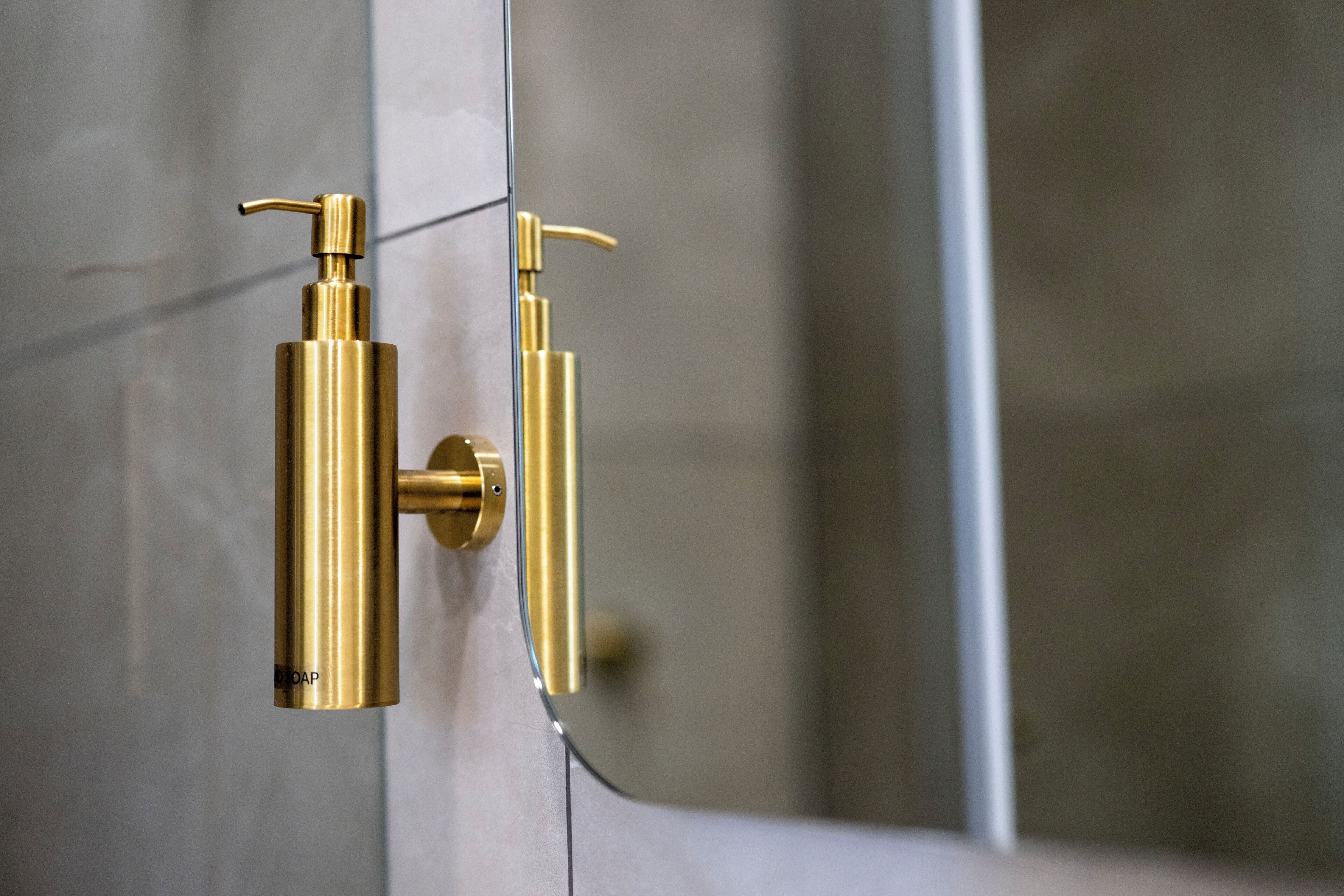 A bathroom with a gold-colored soap dispenser mounted on a glass shower door.