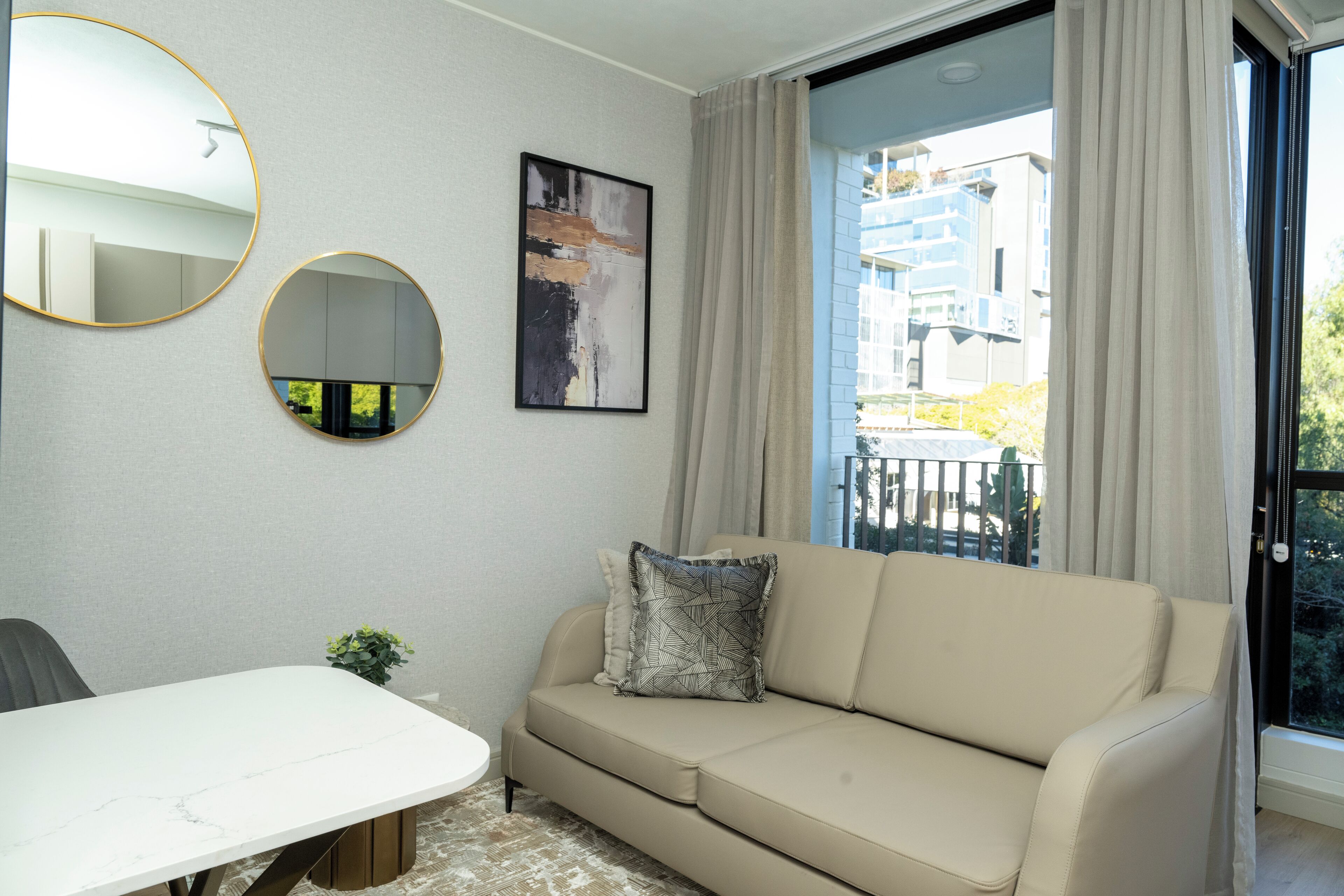 Ein modernes Wohnzimmer mit einem beigen Sofa, einem weißen Esstisch und zwei runden Spiegeln an der Wand.