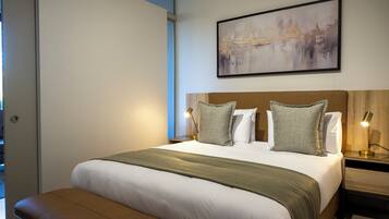 A neatly made bed with a green throw blanket, two bedside lamps, and a framed abstract painting above it.