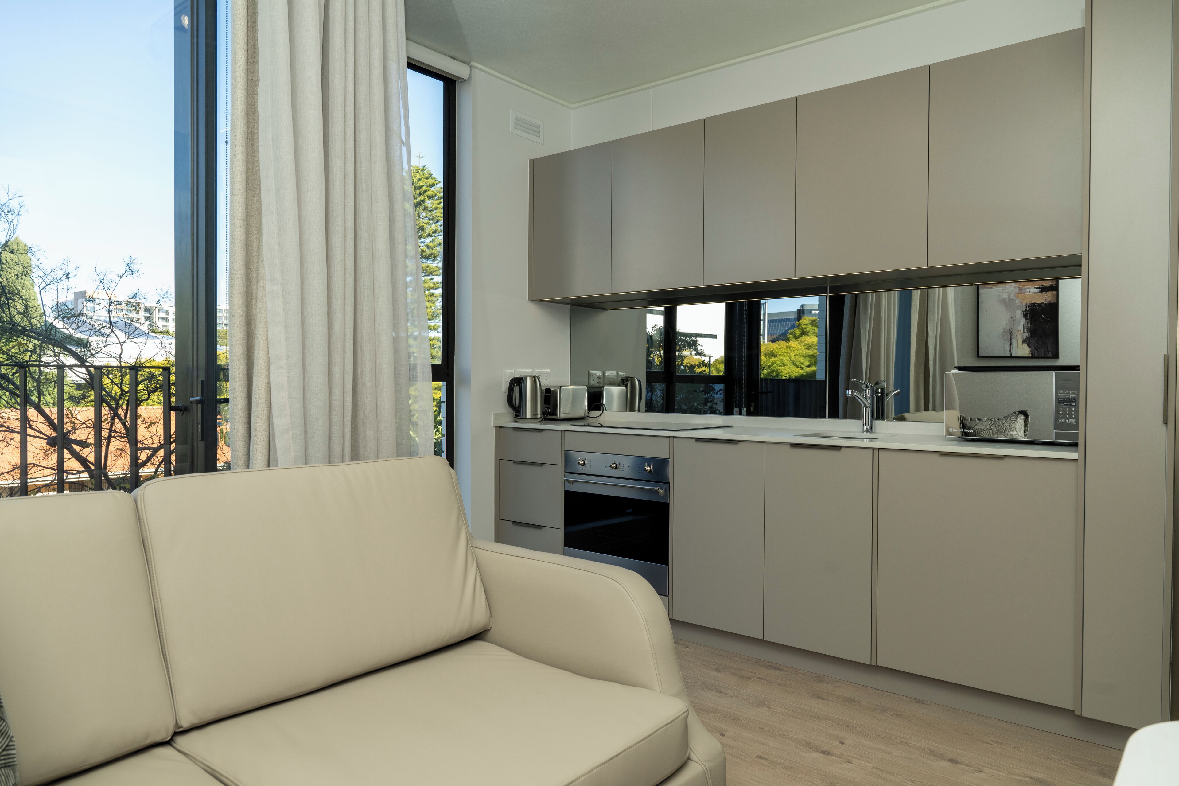 A modern kitchen with a built-in oven and microwave, a dining area with a sofa, and a large window offering a view of the outdoors.