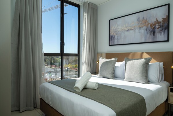 A hotel room with a large bed, a view of a construction site, and a painting on the wall. - One Rosebank Executive Apartment Hotel (Johannesburg)