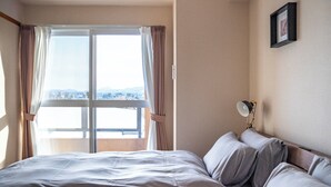 A hotel room with a bed, a nightstand, a lamp, and a window with curtains. - E-US NAEBO1002 (Sapporo)