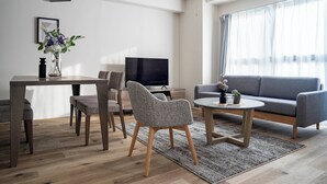 A modern living room with a dining area, grey sofas, a TV, and a vase with flowers. - E-US NAEBO1002 (Sapporo)