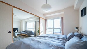 A modern hotel room with a large bed, a desk, and a view of the city through the window. - E-US NAEBO1002 (Sapporo)