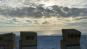 Strandliegen mit den Nummern 1610, 1612 und 1604 an einem sandigen Strand unter einem bewölkten Himmel.
