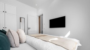 A modern bedroom with a bed, pillows, a TV, and white wardrobes. - Premium vacation apartment in the heart of Westerland on Sylt (Sylt)