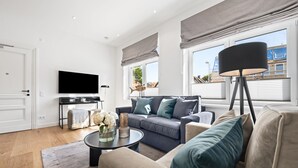 A modern living room with a flat-screen TV, a sofa, a coffee table with decorative items, and large windows with curtains. - Premium vacation apartment in the heart of Westerland on Sylt (Sylt)