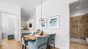 A modern kitchen with white cabinets, a dining area with a wooden table and light blue chairs, and two framed artworks on the wall. - Premium vacation apartment in the heart of Westerland on Sylt (Sylt)