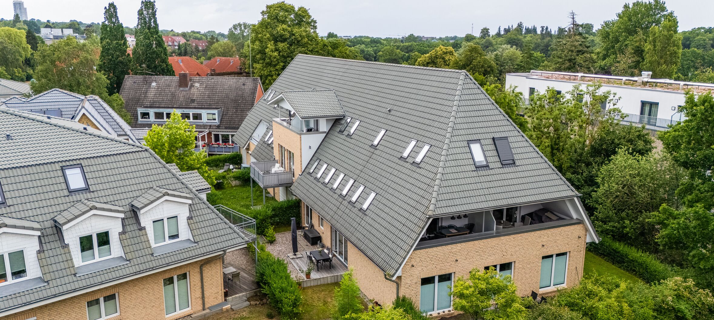 A residential building with multiple roof levels, a patio area with outdoor furniture, and a garden.
