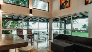 A modern interior with a large glass door leading to an outdoor area, wicker furniture, and a concrete floor. - Marleys Beach House (Talpe)