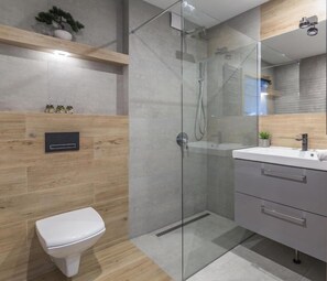 Ein modernes Badezimmer mit einer Duschkabine aus Glas, einer weißen Toilette und einem Waschtisch mit Spiegel.