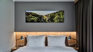 A hotel room with a large bed, two bedside tables with lamps, a wall-mounted TV, and a view of a mountainous landscape. - Hotel Great Polonia Kraków Airport (Modlniczka)