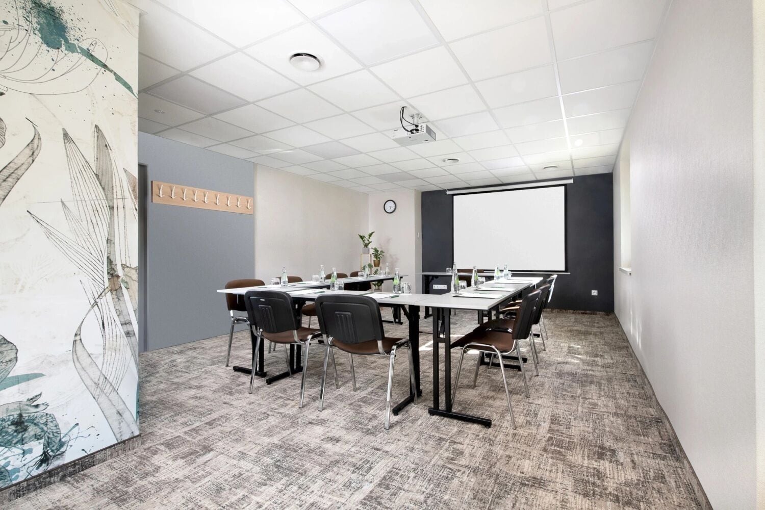 Une salle de conférence équipée d’une grande table, de chaises, d’un écran de projection et d’une horloge au mur.