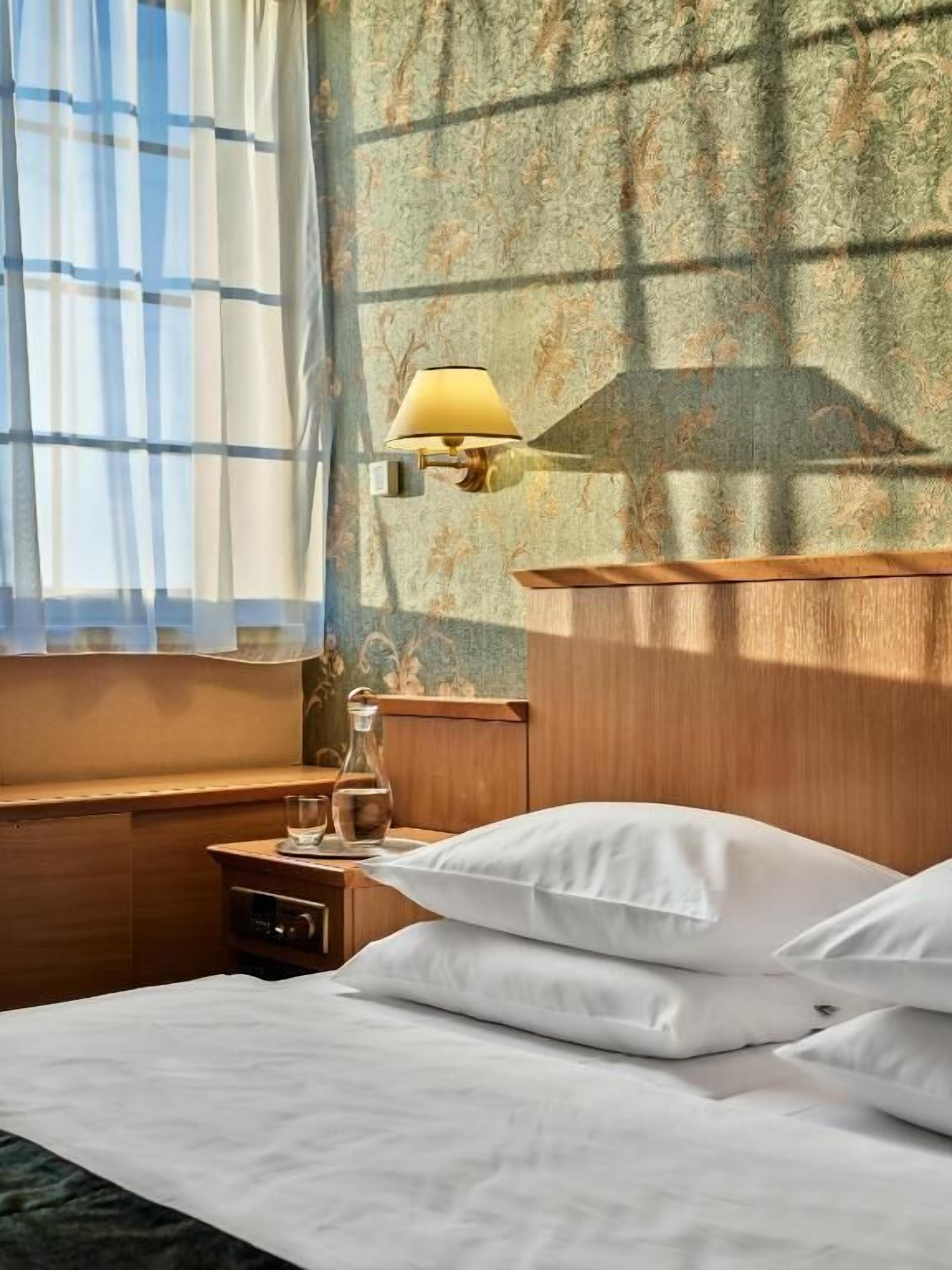 Et hotelværelse med en seng, et natbord, en lampe og et vindue med gardiner.