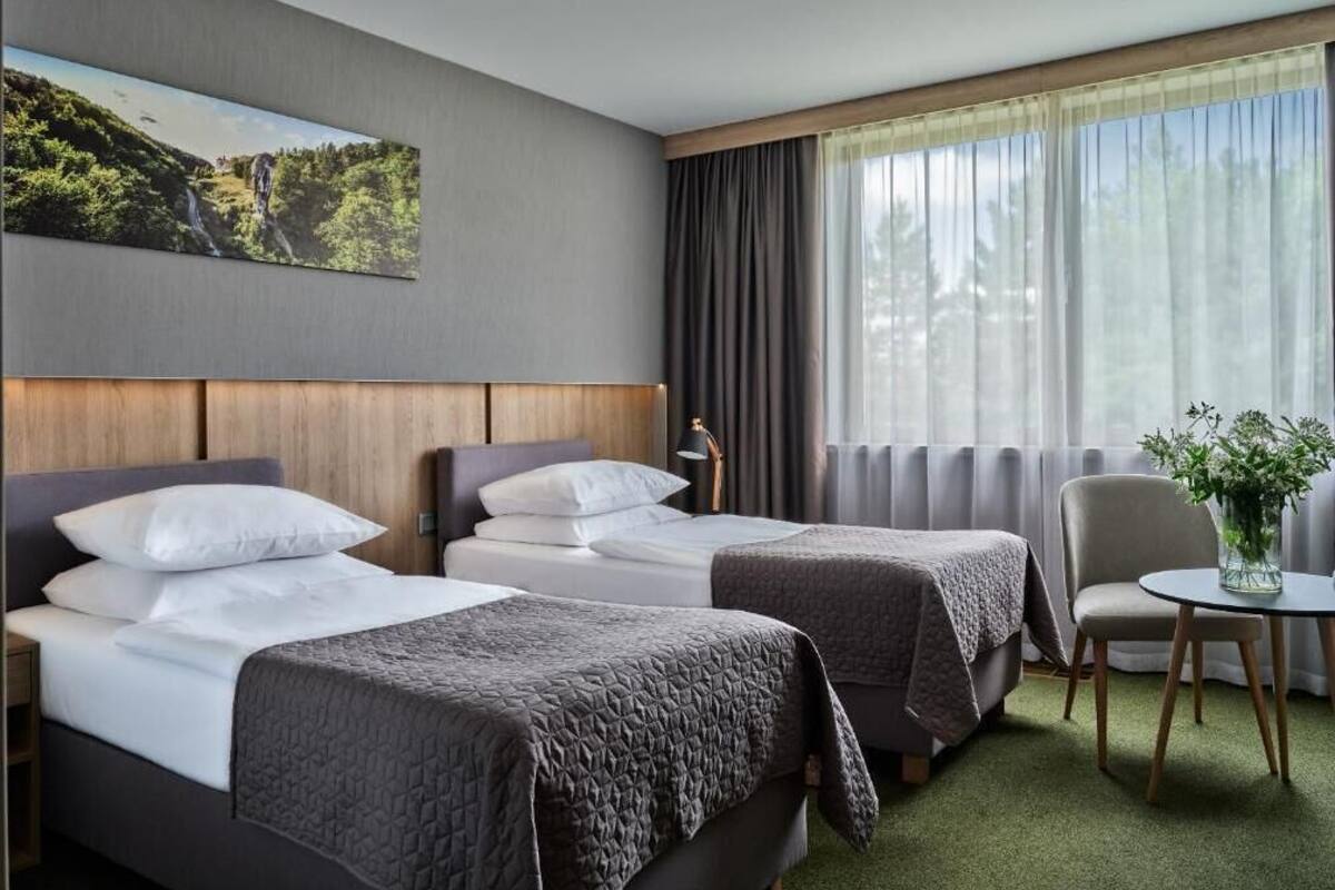 A hotel room with two beds, a small table, a chair, and a painting on the wall.
