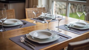 Une table à manger dressée avec des assiettes, des couverts et des verres à vin, entourée de chaises.