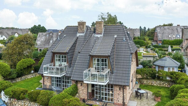 Une grande maison dotée d’un balcon, d’un mur en pierre et d’un jardin bien entretenu.
