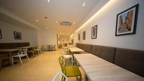 A modern dining area with long tables and chairs, a central walkway, and framed pictures on the walls. - STAY AT 9020 (St. Paul's Bay)