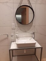 Un baño moderno con un lavamanos rectangular, un espejo redondo y un perchero para toallas.