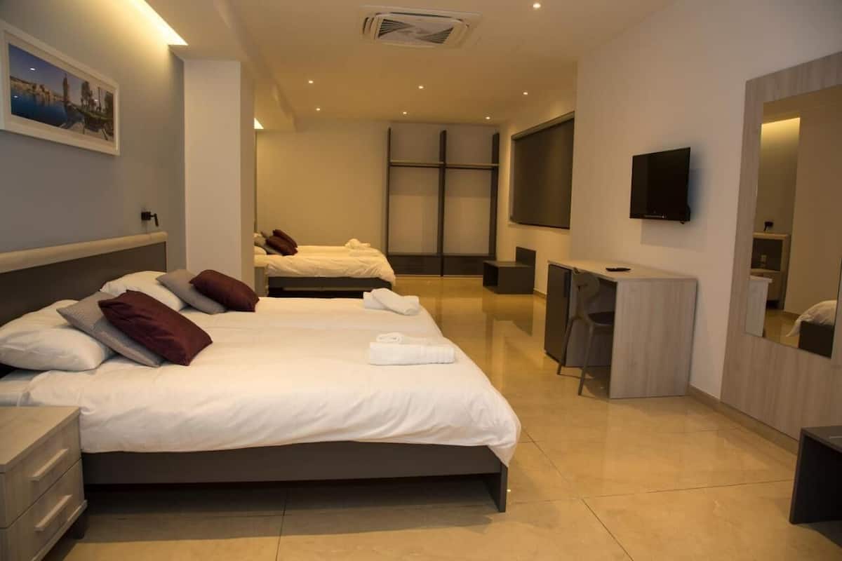 Ett modernt hotellrum med två sängar, ett skrivbord, en TV och ett stort fönster.
