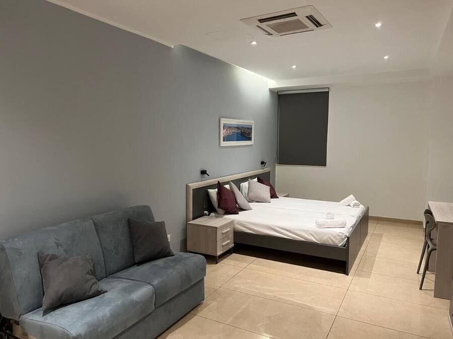 Un dormitorio moderno con cama, sofá gris, mesita de noche y escritorio.