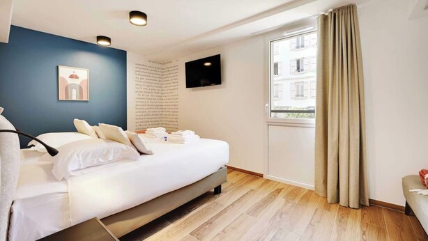 Et moderne hotelværelse med en seng, et fladskærms-tv, et vindue med gardiner og et kunstværk på væggen.
