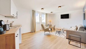 Et moderne køkken med træbordplade, kaffemaskine og elkedel. Der er et spiseområde med bord og stole, samt en sofa i opholdsstuen.