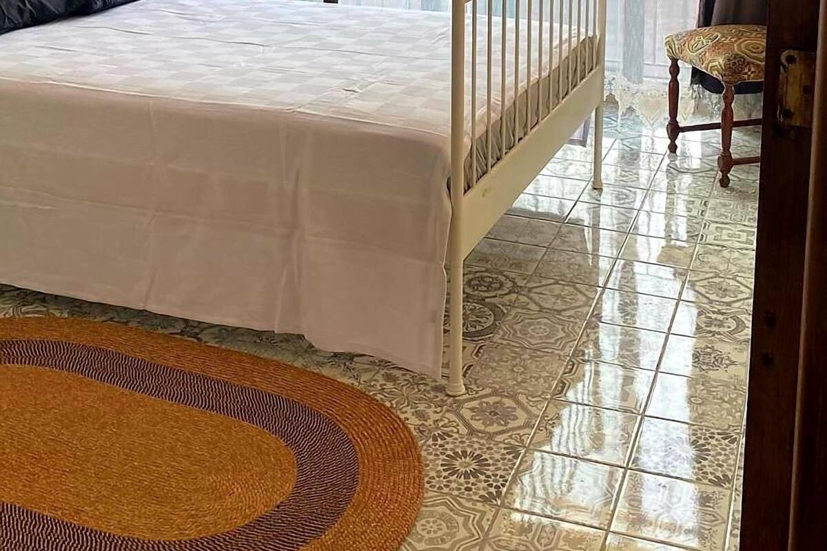 Une chambre à coucher avec un lit, une chaise, une fenêtre avec des rideaux et un sol à motifs.