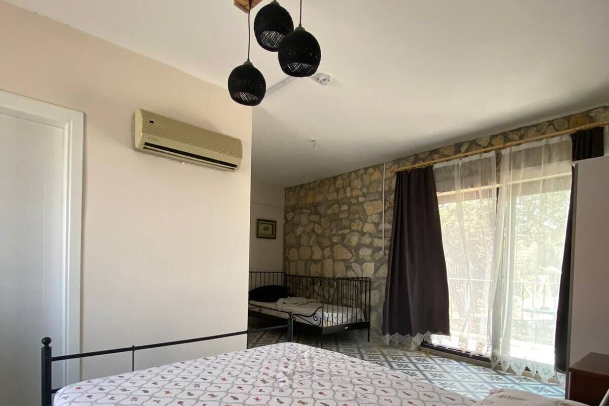 Une chambre à coucher comprenant un lit, un climatiseur, un mur en pierre, une fenêtre avec des rideaux et un luminaire suspendu.