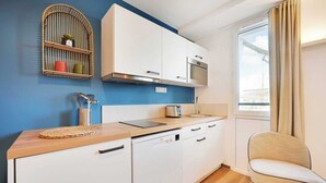 A compact kitchen with white cabinets, a built-in microwave, and a window with curtains. - Appartement Marcel #31 - Rooftop & Air Conditioning (Unknown)