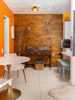 Une cuisine compacte avec un mur en bois, une table à manger blanche et un four à micro-ondes placé à droite.