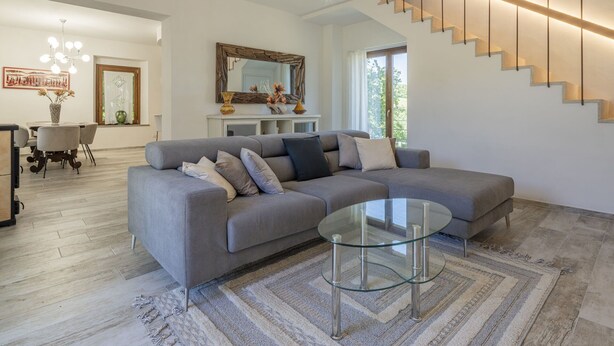 Un salon moderne avec un canapé d’angle gris, une table basse en verre et un escalier avec des marches en bois.