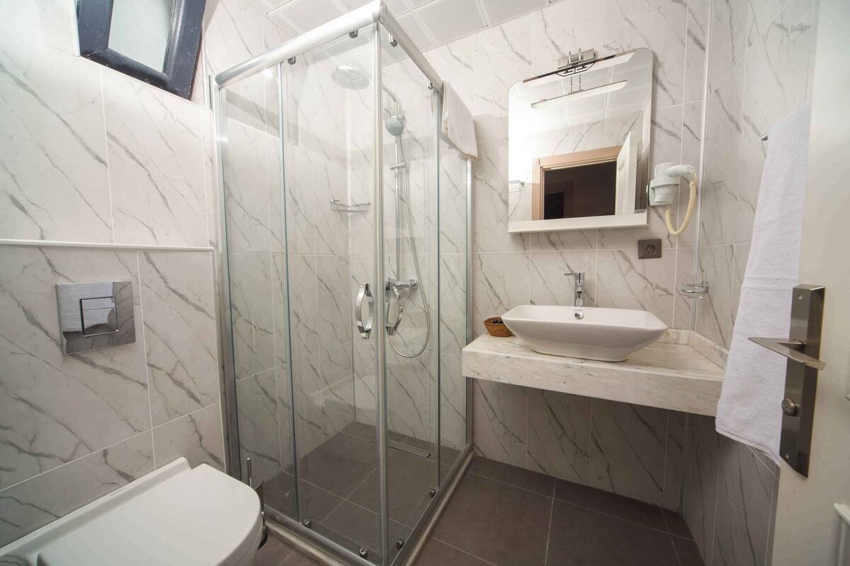 A modern bathroom with a glass-enclosed shower, a white sink, and a marble-tiled wall.