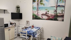 Comedor con mesa para cuatro, televisor montado en la pared y un cuadro de una playa tropical.