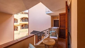 Un balcón con mobiliario de mimbre, vistas a edificios cercanos y una puerta de madera.