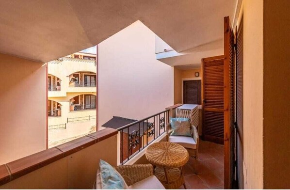 A balcony with wicker furniture, a view of neighboring buildings, and a wooden door.