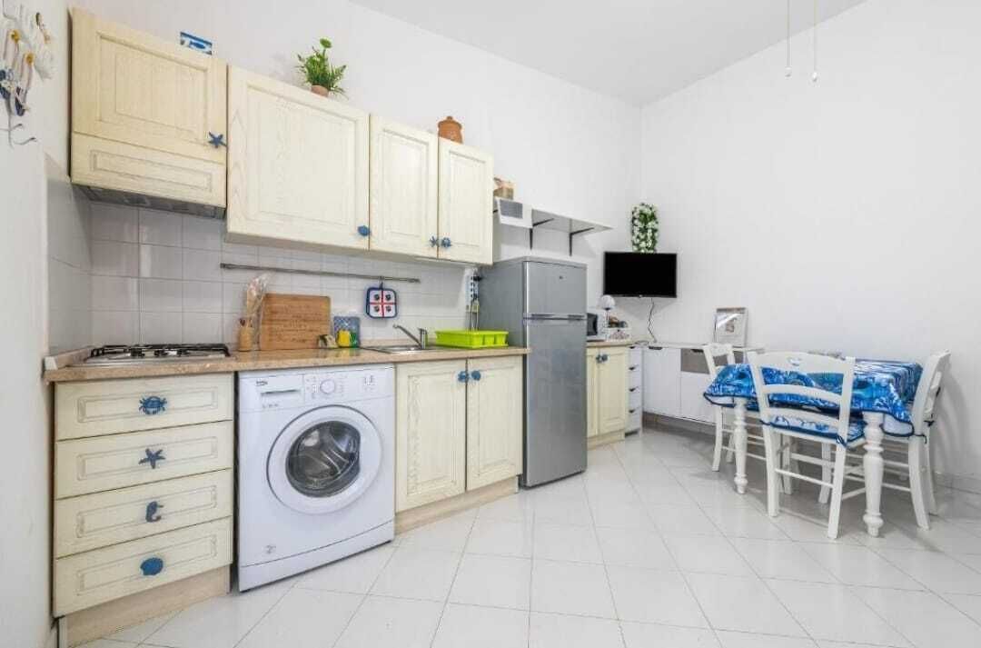 A compact kitchen with white cabinets, a washing machine, a refrigerator, and a dining area with a table and chairs.
